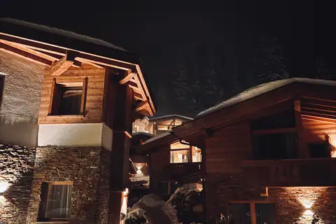 Stone and timber mountain home lit up on a snowy night